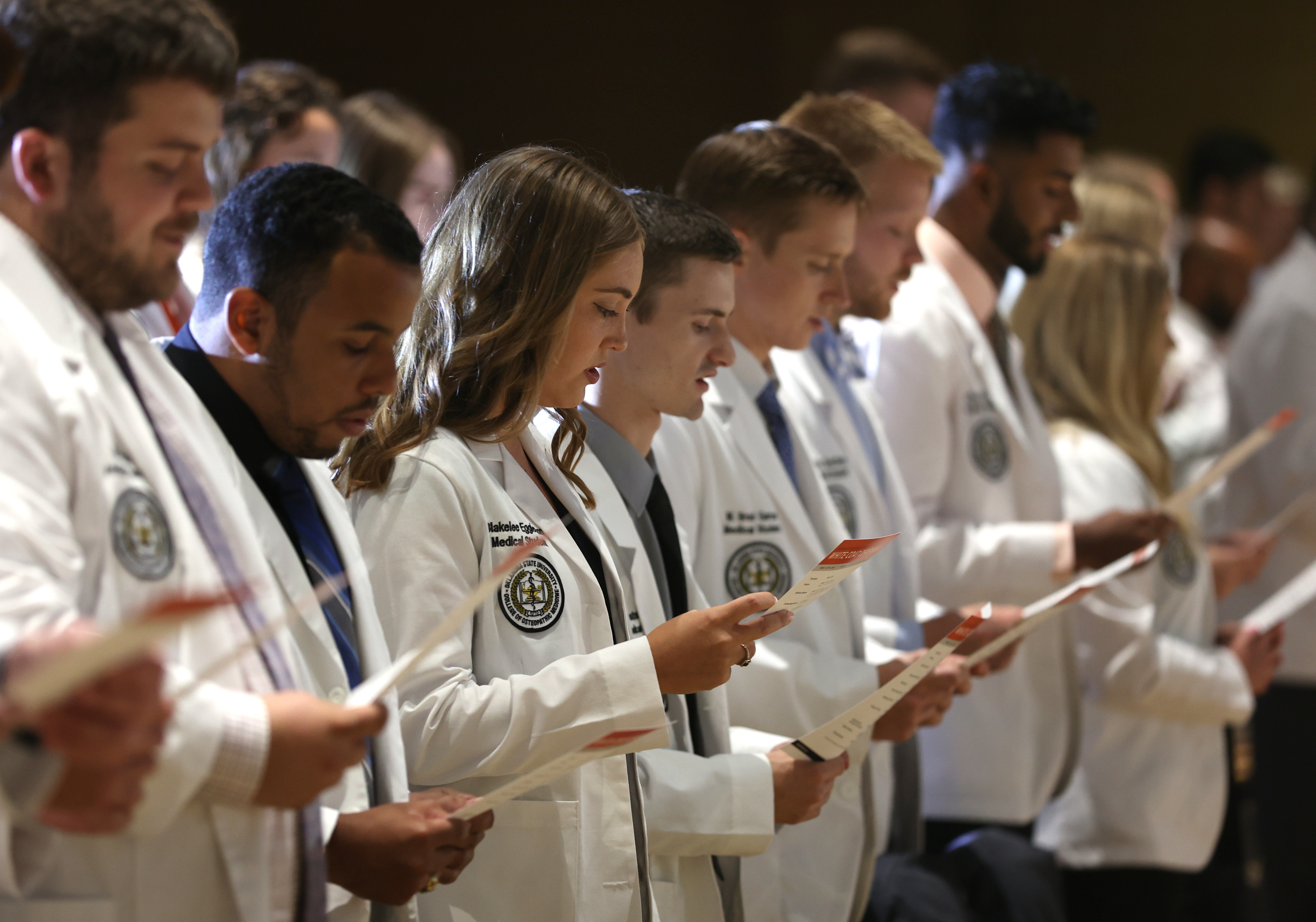 Students in white coats at Oklahoma State University College of Osteopathic Medicine reading from a pamphlet