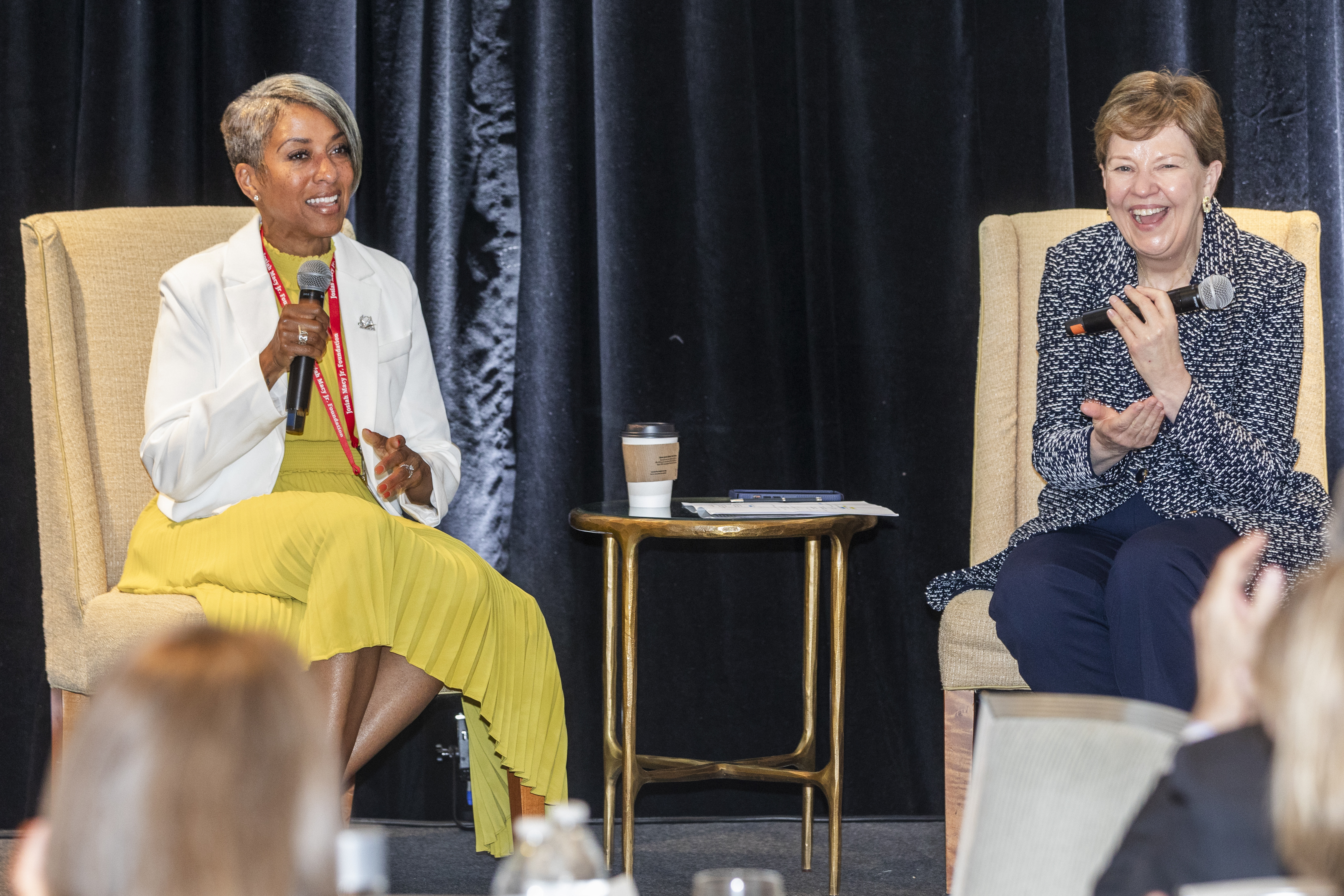 Dr. Kimberly Manning and Dr. Holly J. Humphrey are sitting opposite one another in chairs on a stage holding microphones with a table in between them.