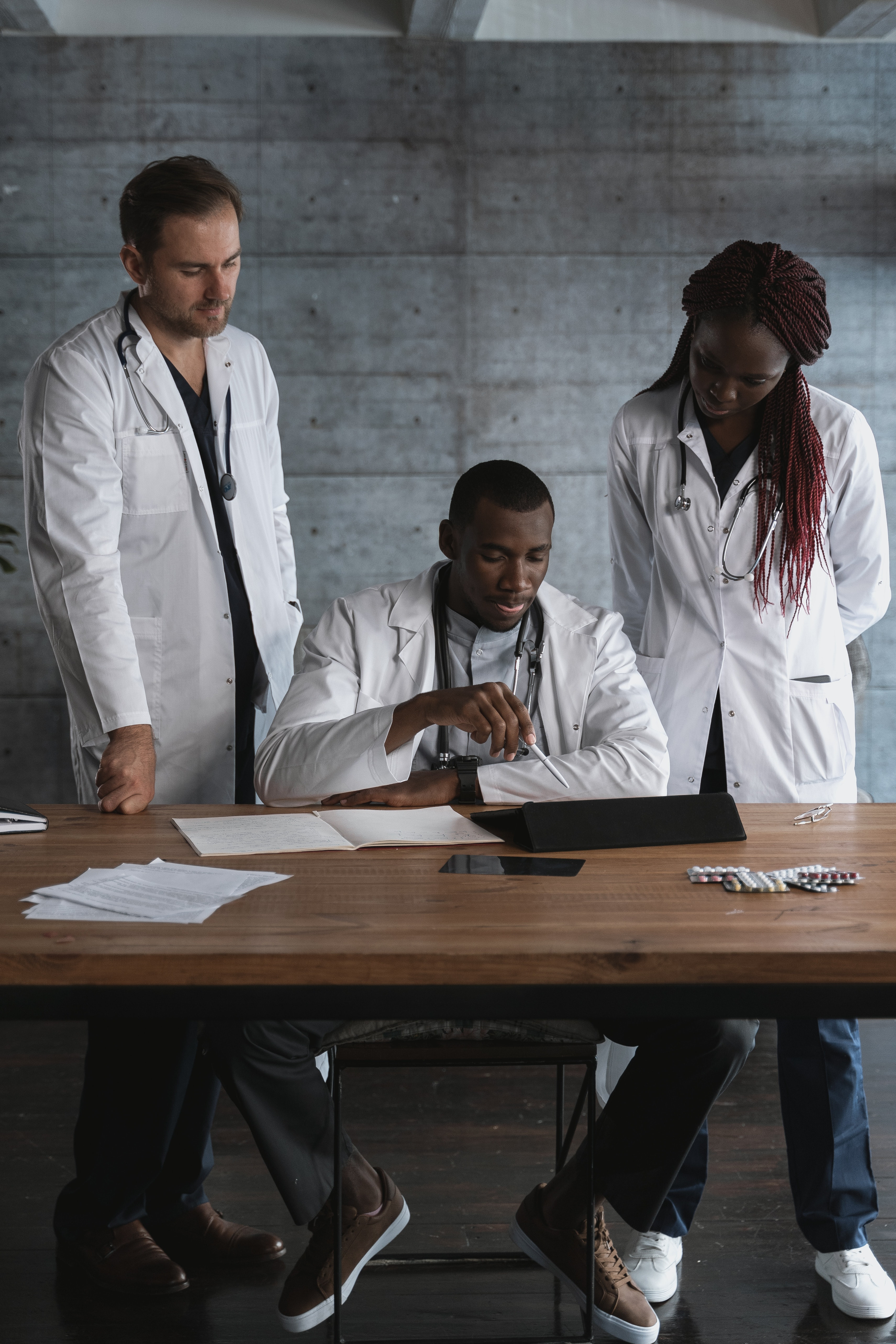 Three medical students in white lab coats collaborate on work around a table