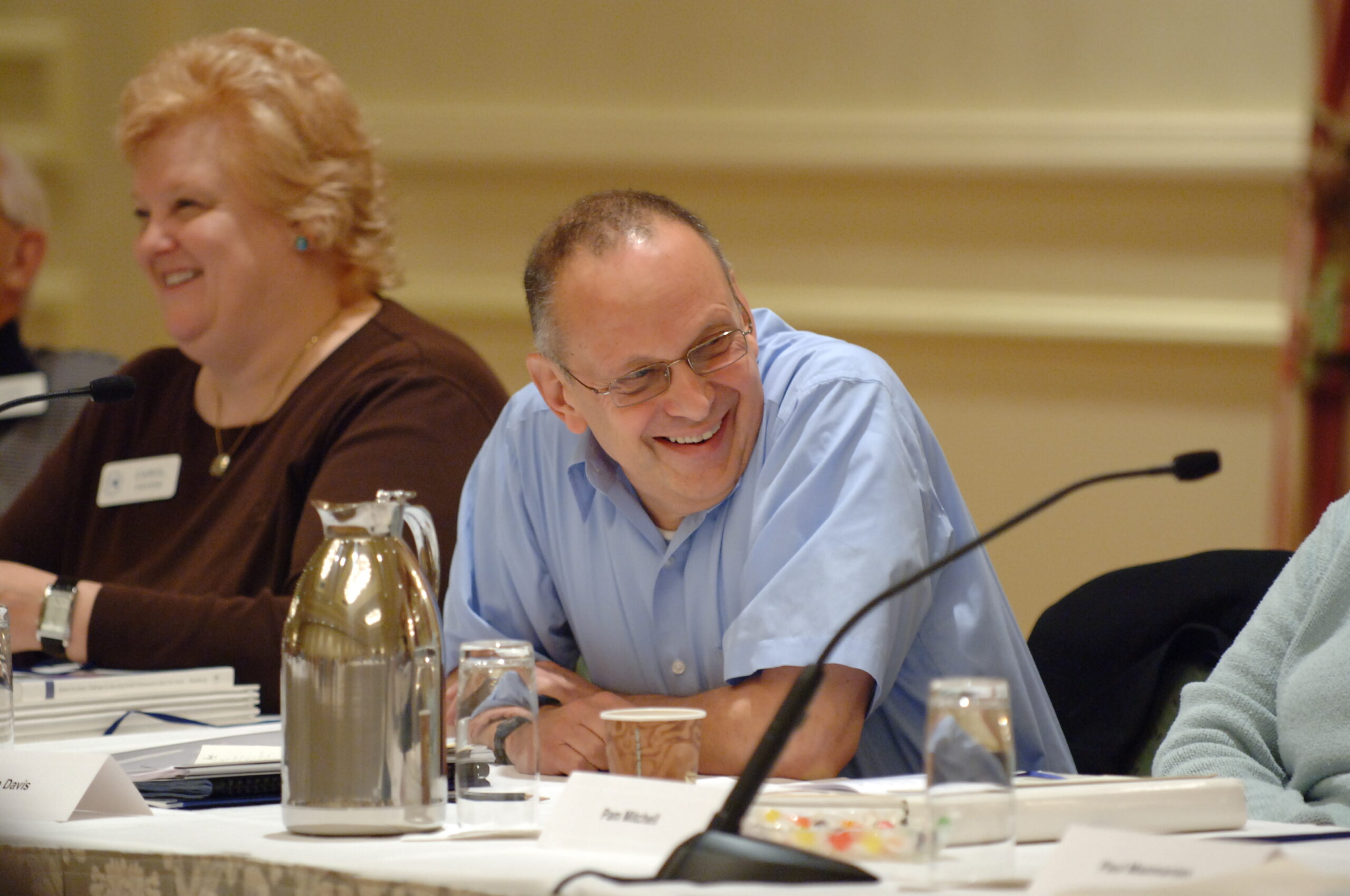 A man in a blue shirt smiles at a conference table