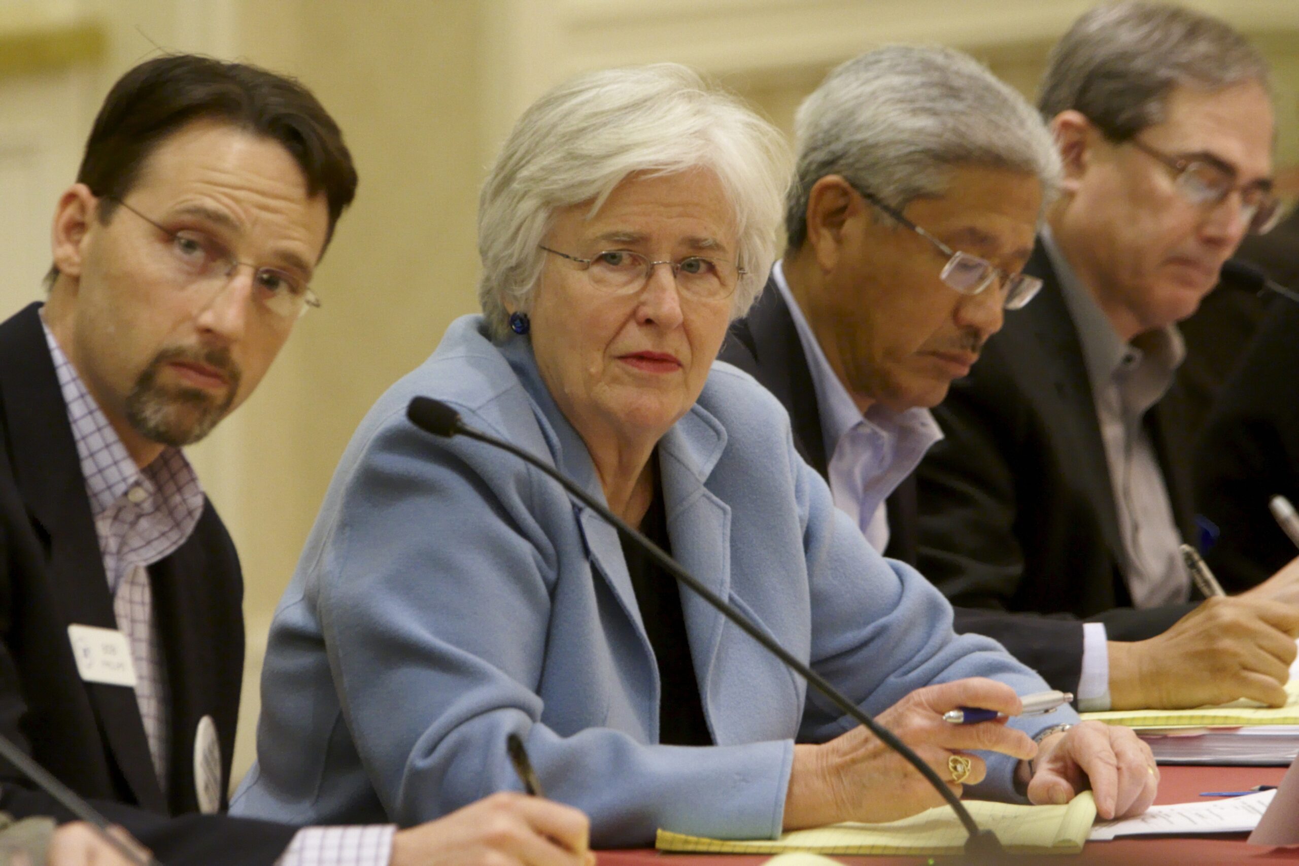 A panel photo of conference attendees sitting at a table with microphones in front of them
