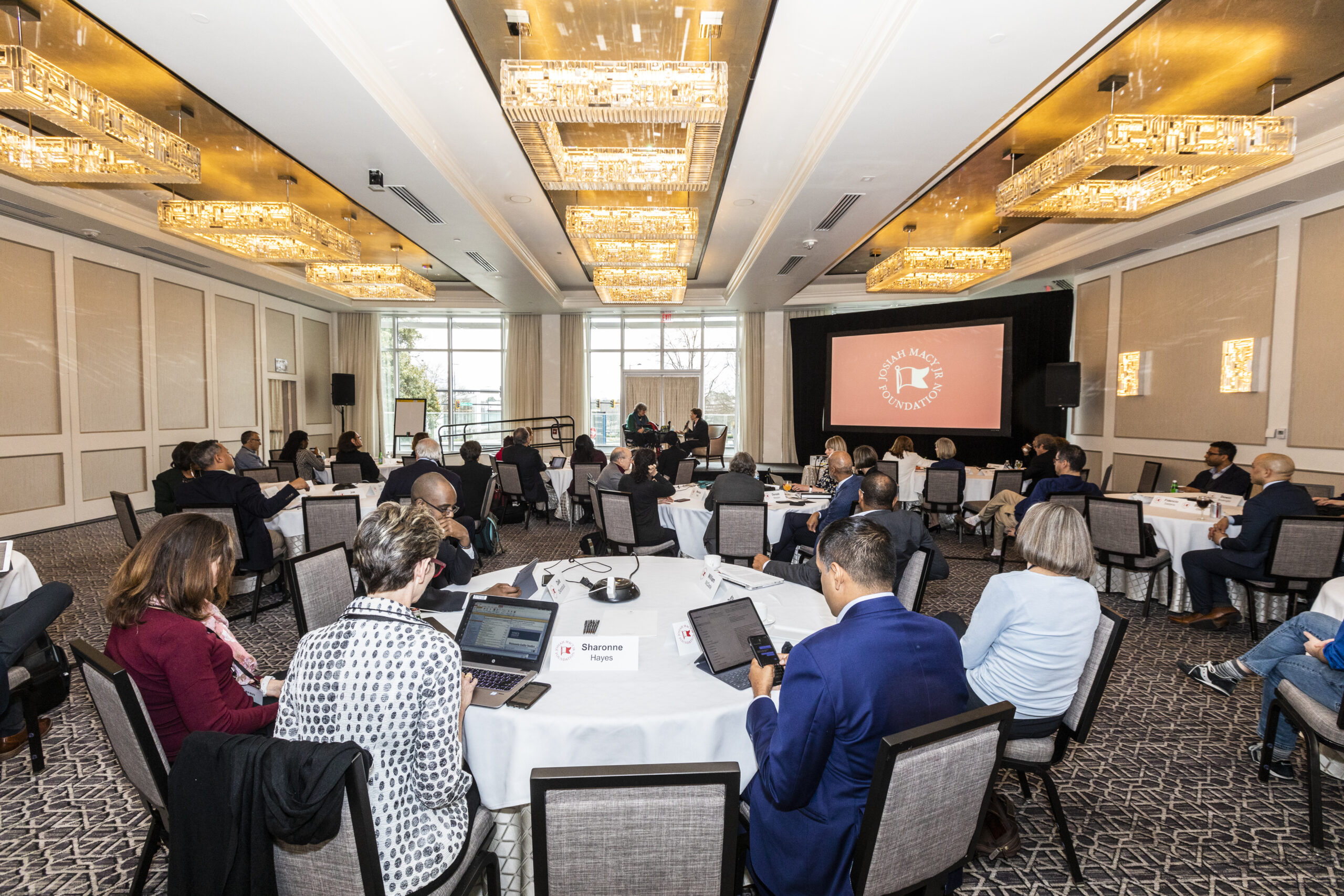 A picture of a conference room with tables and attendees